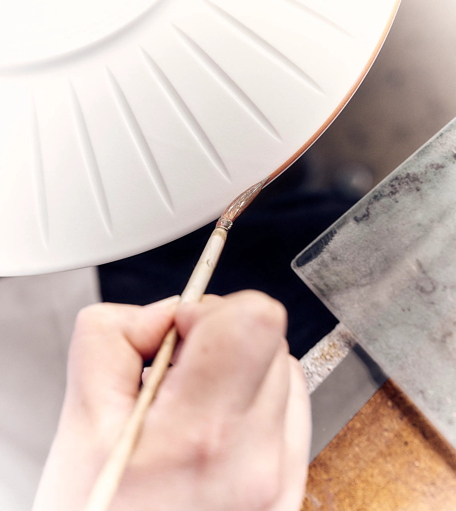 Un artisan applique à la main un filet doré sur une assiette Louis XIII Ode au temps, illustrant une vaisselle de prestige au savoir-faire artistique et au luxe durable.