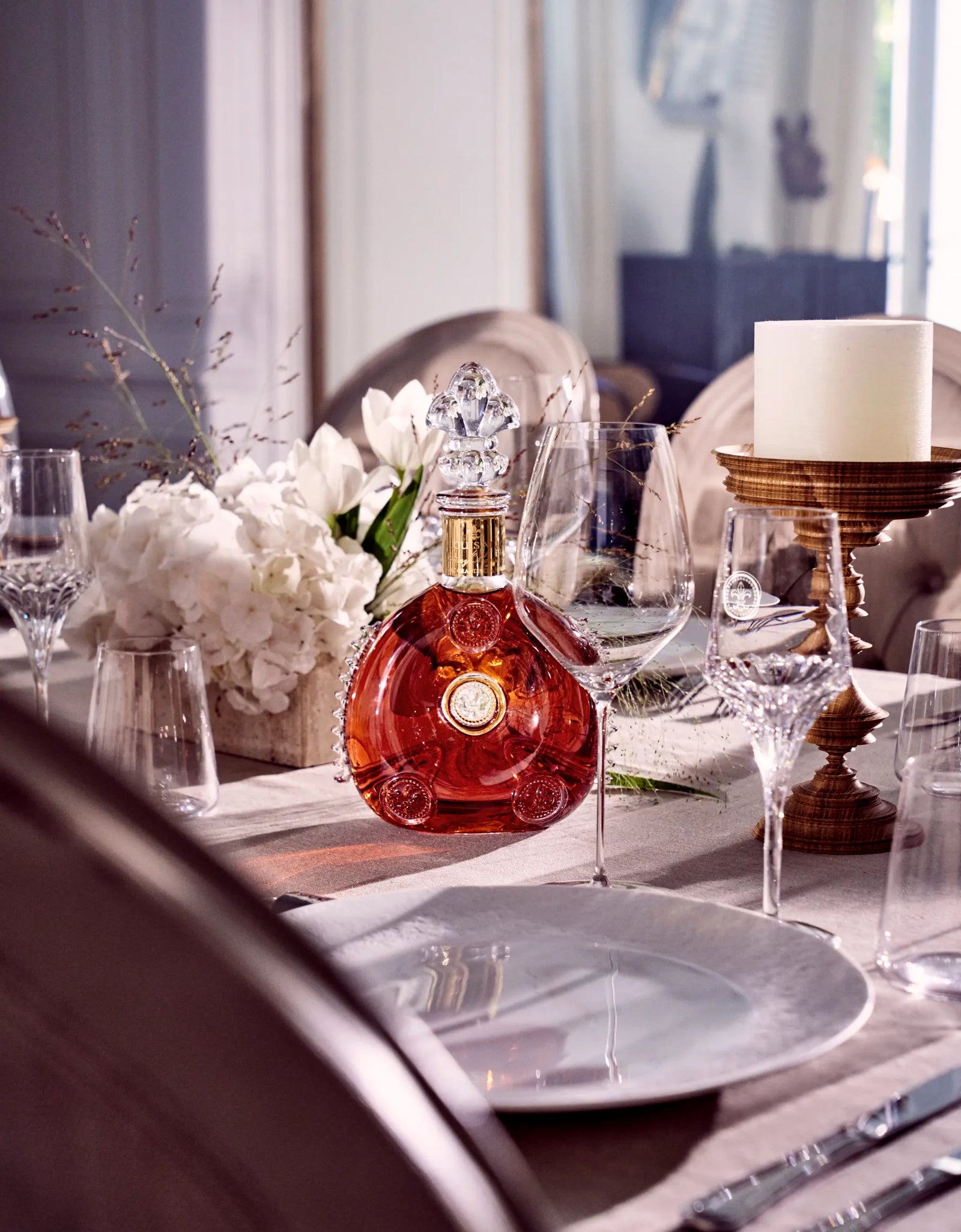 Bouteille de cognac Louis XIII entourée de verres en cristal, d’un bouquet et d’une bougie